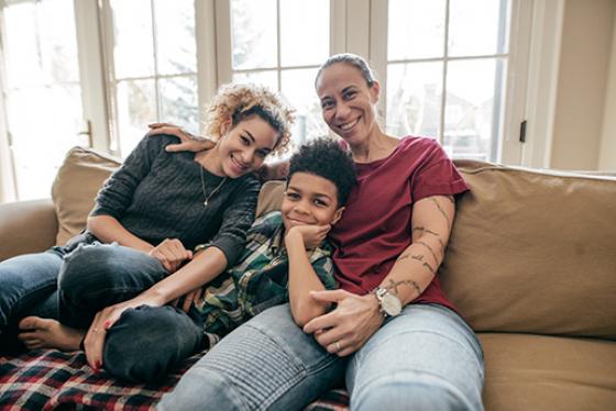 An adult, adolescent, and child sit on a couch and smile.