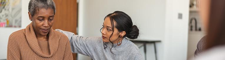 A younger woman comforts an older woman during a support group meeting.