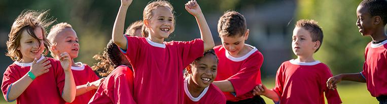 Young boys and girls in red jerseys celebrate on a soccer field.