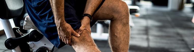 A man sitting at a weight machine grabs his knee in pain.