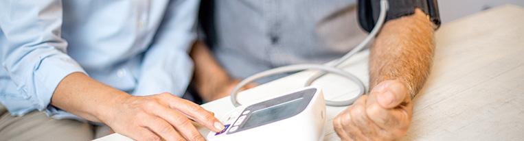 A woman helps a man use a blood pressure cuff to check his blood pressure.