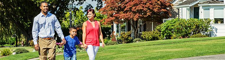 Two parents hold hands with their young son as they walk down a residential sidewalk.