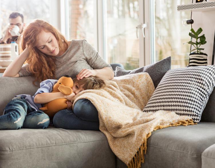 Mother sitting on the couch with a child sleeping in her lap.