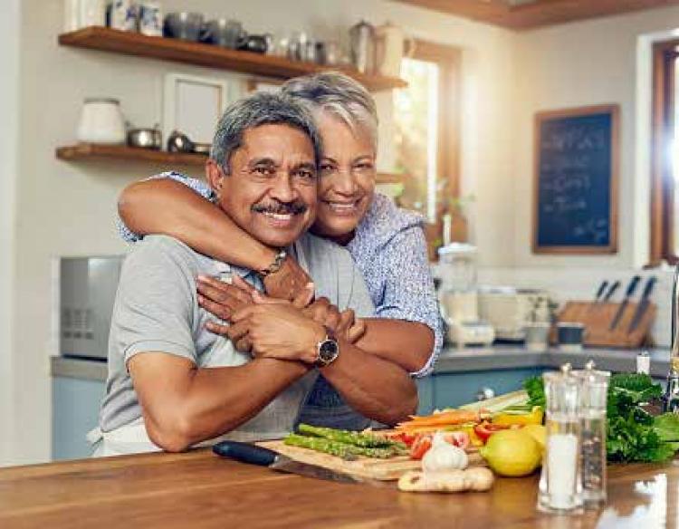 A couple hugs in their kitchen while smiling towards the camera.