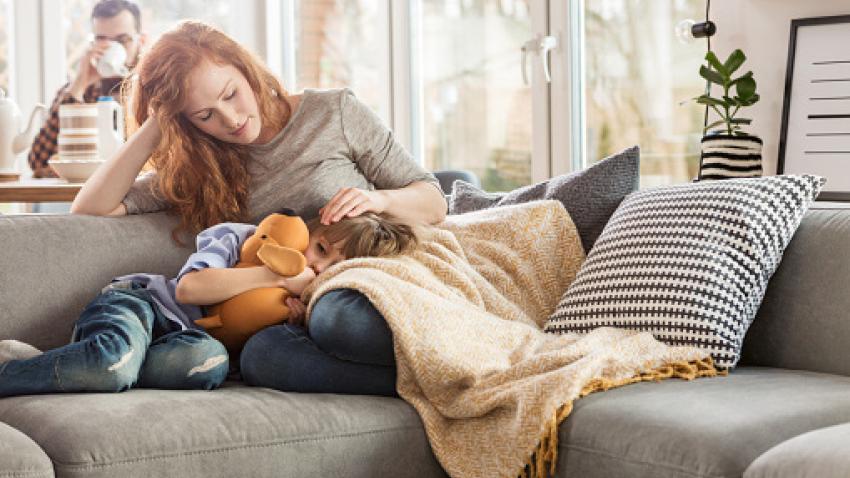 Mother sitting on the couch with a child sleeping in her lap.