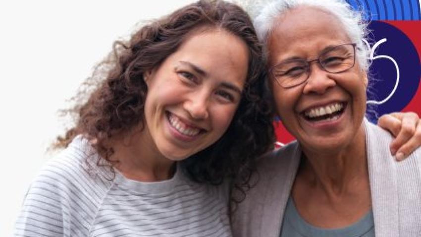 A younger woman smiles and places her arm around a laughing older woman.